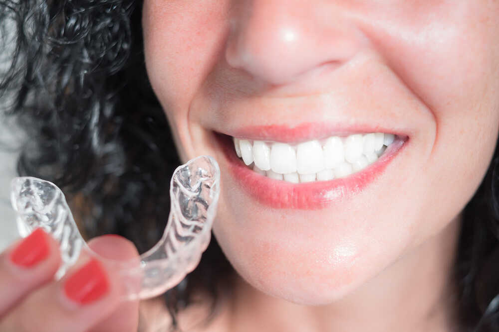 Kobieta z białymi zębami pokazuje nakładki Invisalign